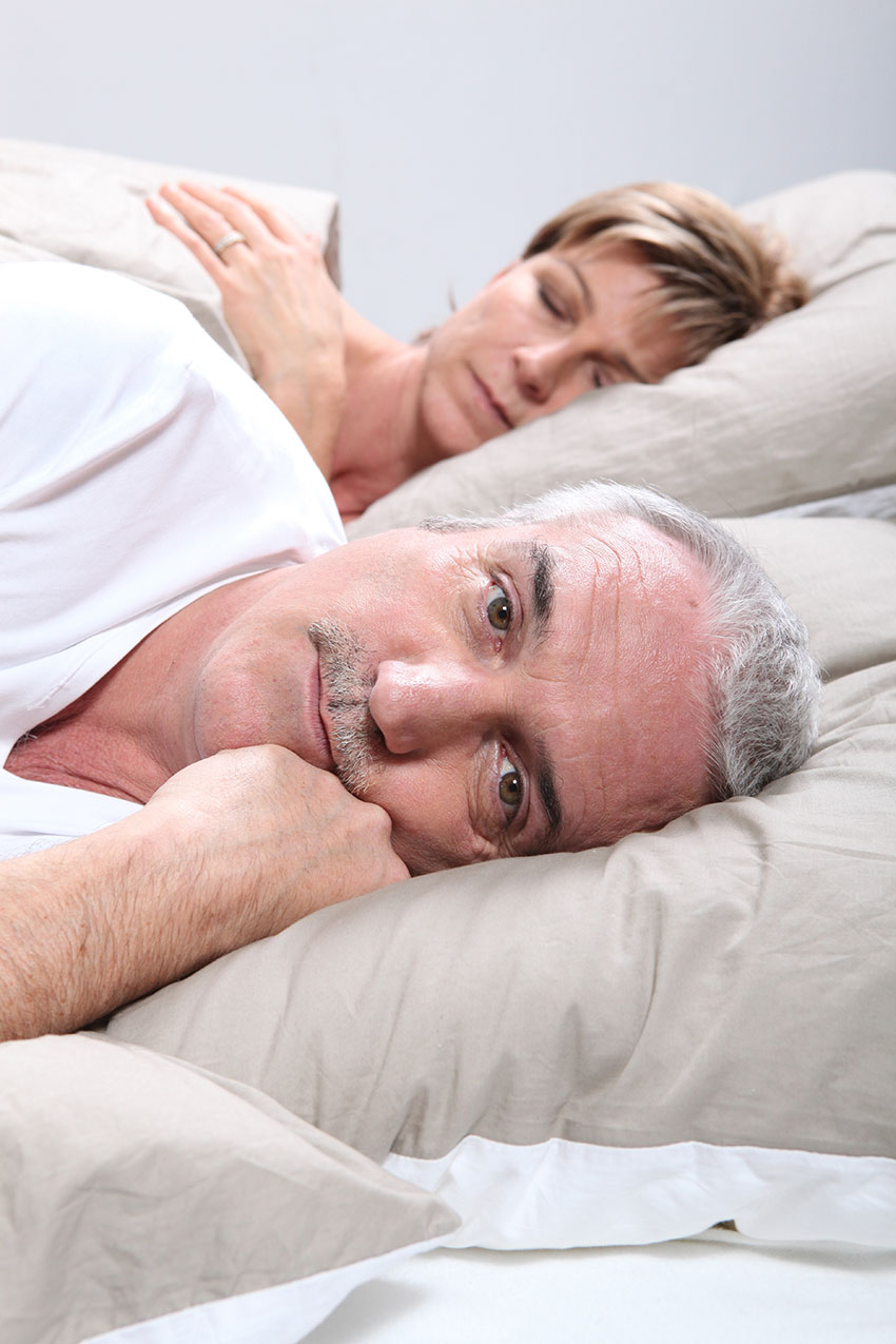 older man unable to sleep stares forward while wife sleeps next to him