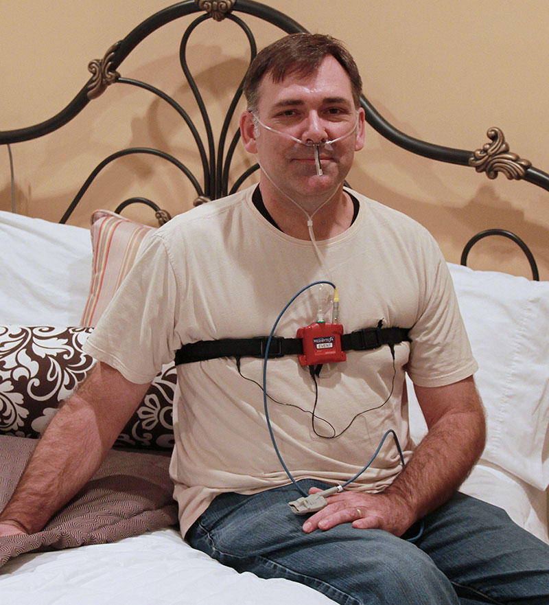 man with home sleep testing device sitting on a bed